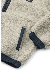 Krémová fleecová bunda s textúrovanou tkaninou, námorníckymi elastickými manžetami, zipsovou kapsou a prešitými švami. Zloženie zahŕňa mäkký, teplý materiál.