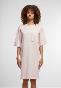 Rochie scurtă cu mânecă scurtă de culoare roz pal, confecționată dintr-un material moale, având un buzunar în față și o croială lejeră, ajungând până la jumătatea coapsei.