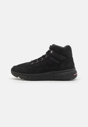 Czarne zamszowe sneakersy za kostkę z metalowymi oczkami, wyściełanym kołnierzem i teksturowaną gumową podeszwą z oznaczeniem marki na pięcie.