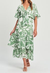 Vestido maxi en estampado floral verde y blanco, con escote en V, lazo en el frente, mangas cortas y volantes en la parte inferior.