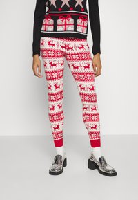 Red and white patterned leggings with reindeer and geometric designs, featuring a fitted shape and ribbed cuffs. Worn with silver loafers.