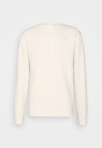 Světlé béžové mikina s dlouhým rukávem z měkké látky. Má žebrovaný kulatý výstřih a malý vystouplý logo na levé horní straně.