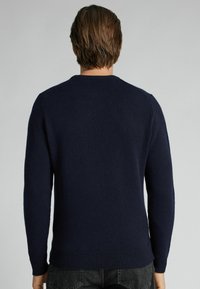 Suéter de punto azul marino con cuello redondo, mangas largas y dobladillo y puños acanalados. El material parece suave y texturizado.