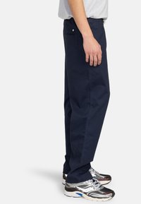 Mørkeblå bomuldsbukser med lige ben-design, der har sidelommer og en baglomme med knap. Sammen med metalliske sneakers.