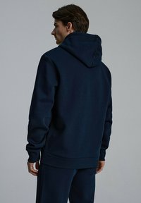 Granatowa bluza z kapturem wykonana z miękkiego materiału, z kapturem ze sznurkiem i ściągaczami przy mankietach, o luźnym kroju, bez widocznych logo ani wzorów.