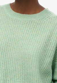 Ljusgröna stickade tröjan med rund halsringning, texturerad tyg och avslappnad passform. Garnet verkar mjukt med en lätt färgavvikelse.