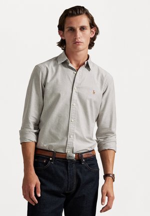 Light gray button-up shirt with long sleeves, featuring a small logo, paired with dark blue jeans and a brown leather belt.