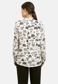 Long-sleeve blouse in cream fabric, featuring a black graphic print of pots and patterns. Structured fit with buttoned cuffs and back pleat.