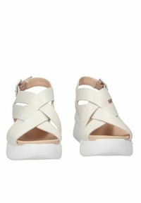 Sandali platform bianchi con cinturini incrociati, tacco aperto e una texture liscia. Presentano una suola bianca solida e un rivestimento interno beige.