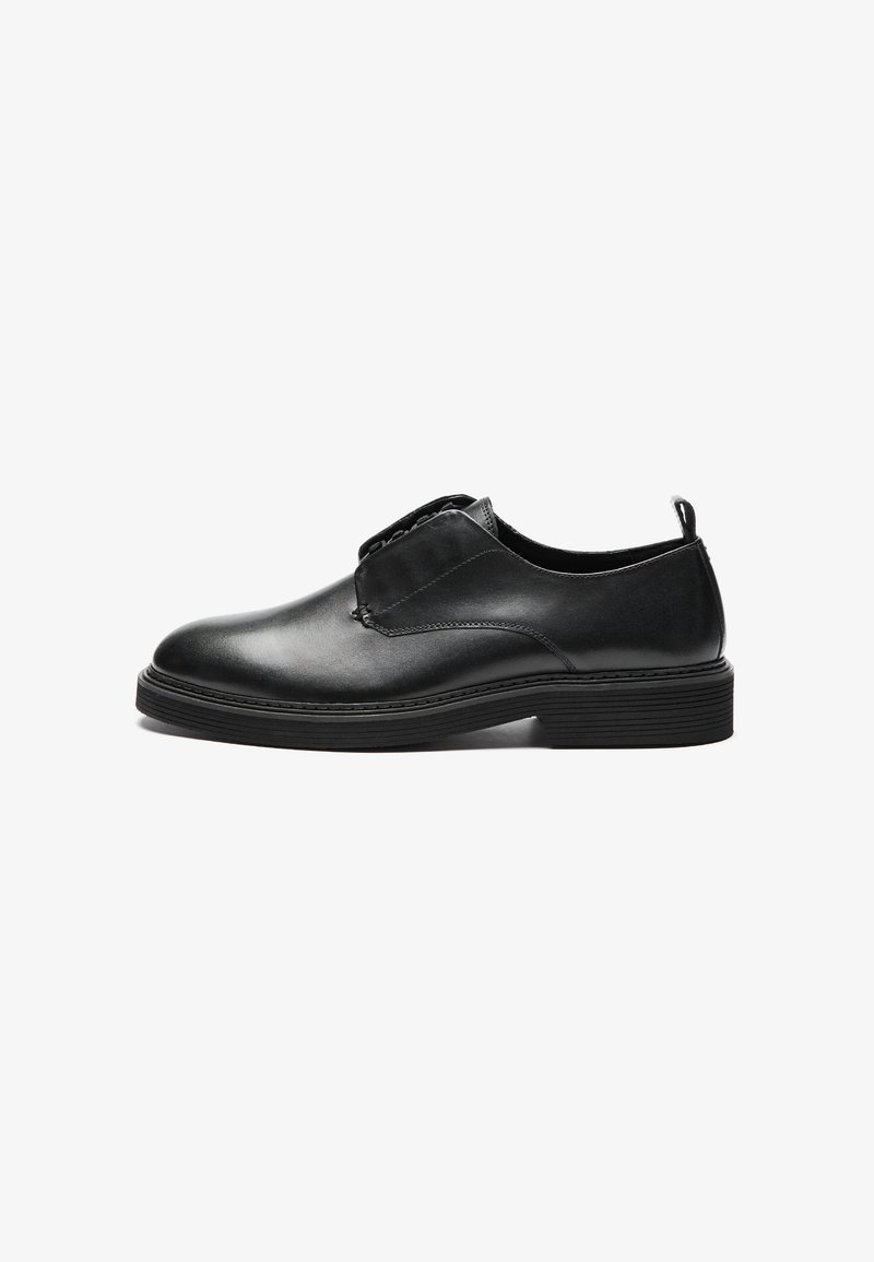 Zapato de cuero negro con un acabado suave, punta redonda, paneles laterales elásticos y una suela de goma estriada. Diseño minimalista con costuras sutiles.
