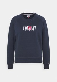 Felpa blu navy con scollo rotondo e polsini a costine. Presenta il logo "TOMMY JEANS" ricamato in bianco e rosso. Tessuto dalla texture morbida.