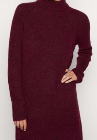 Burgundy polokrage tröja, tillverkad av mjukt stickat material, med långa ärmar och en avslappnad passform, med en subtil textur och detaljer vid muddarna.