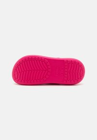 Suela de zapato de color rosa brillante con un patrón de relieve texturizado y el logotipo de la marca estampado en el centro sobre un fondo blanco liso.