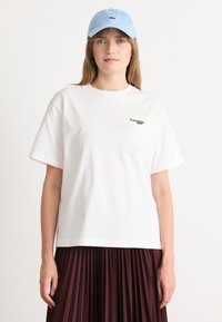 Hvit bomulls T-skjorte med rund hals og korte ermer, med en grønn brodert logo. Sammen med en lys blå caps.