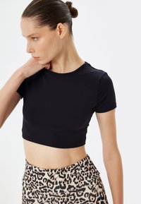 Sort cropped t-shirt med korte ærmer; glat tekstur. Kombineret med højtsiddende leggings med leopardprint, der har et blødt, strækbart materiale.