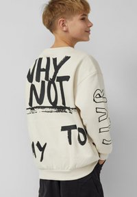 Roomkleurige sweatshirt met opvallende zwarte tekst en grafische accenten. Losse pasvorm met geribbelde boorden en zoom, gemaakt van zachte stof.