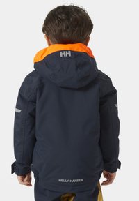 Námořnická voděodolná bunda s oranžovou kapucí, šedými akcenty a nastavitelnými manžetami. Na zadní straně je umístěno logo značky a reflexní detaily.