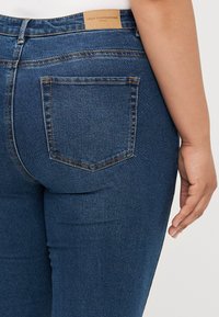 Jeans de mezclilla azul oscuro con una textura suave, que cuentan con una etiqueta de cuero en la cintura y dos bolsillos traseros con costuras en contraste.