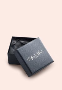 Boîte à bijoux noire en texture avec un logo argenté, légèrement ouverte pour révéler du papier noir froissé à l'intérieur. Forme carrée avec une surface lisse.