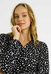 Camisa negra de botón con un patrón texturizado de formas abstractas en blanco y dorado. Tejido suave con cuello y mangas largas.