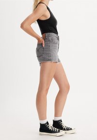 Shorts de mezclilla gris con dobladillo deshilachado, de cintura alta y dos bolsillos frontales. Combinados con una camiseta negra sin mangas y zapatillas altas negras.