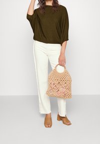 Olijfgroene gebreide top, witte wijde jeans en een tan geweven handtas met een ronde handgreep. Bruine open-toed hoge hakken sandalen.