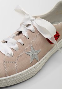 Jasnoróżowy tenisówka z płótna z białymi satynowymi sznurowadłami, srebrnym haftem gwiazd i naszywką w kształcie czerwonych ust. Biała gumowa podeszwa z teksturowanym uchwytem.