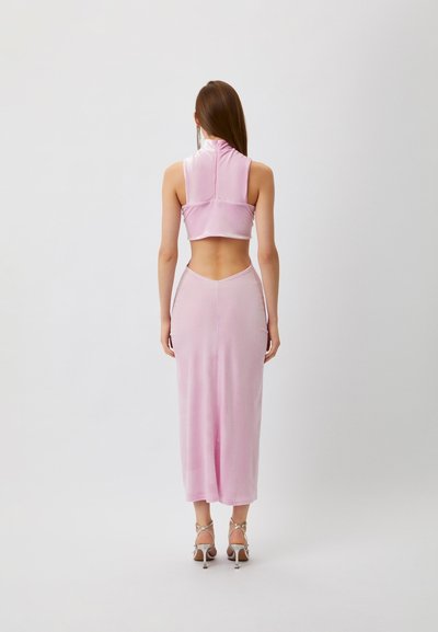 Rosa, ärmelloses Cropped Top mit hohem Kragen, kombiniert mit einem enganliegenden langen Rock mit einem Schlitzausschnitt hinten. Material ist glatt und glänzend. Silberne Absätze.