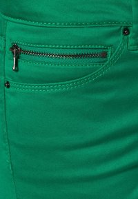 Groene, rekbare spijkerbroek van stof met een zijrits zak, voorzien van metallic zilveren hardware en contrasterende stikdetails.