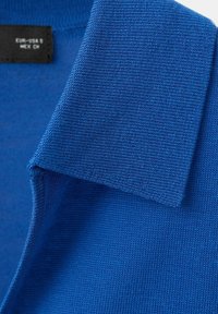 Guler de tricou polo albastru, cu textură vizibilă a materialului și o etichetă de mărime neagră în interiorul gâtului.