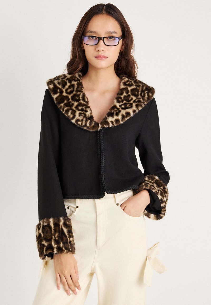 Casaco preto cropped com colarinho e punhos em pelagem sintética com padrão de leopardo, apresentando um acabamento texturizado e um fecho frontal com costura decorativa.