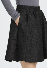 Black skirt with a floral embossed pattern, gathered elastic waistband, and side pockets. Fabric appears textured and lightly structured.