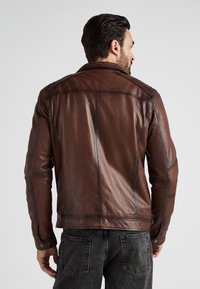 Brun læderjakke med en glat overflade, der har en tætsiddende design, detaljerede sømme og trykknapper ved ærmerne.