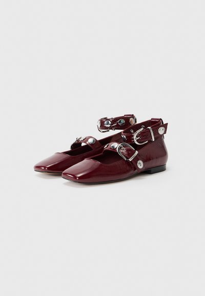 Burgundy patent leather flats with ankle straps, silver hardware buttons, and a square toe design. Flat sole with minimal elevation.