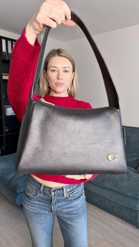 Μαύρη δερμάτινη τσάντα ώμου με υφή, καμπυλωτή κορυφή, χρυσά αξεσουάρ και φαρδύ λουρί, τοποθετημένη σε ουδέτερο φόντο.