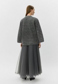 Chaqueta gris acolchada de corte holgado, combinada con una falda larga de tul gris semitransparente. Presenta mangas anchas y un dobladillo recto.