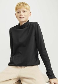 Must mustlastik turtleneck, mis on valmistatud pehmest kangast, lõdva lõike ja sileda tekstuuriga, kombineeritud heledate kootud pükstega.