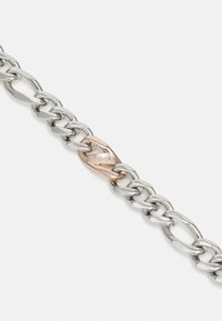 Pulsera de cadena de metal en tono plateado con eslabones entrelazados, y un cierre central en oro rosa grabado con el nombre de la marca "BOSS."
