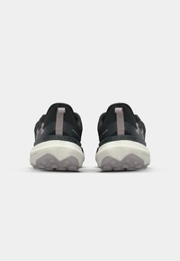 Baskets de sport noires avec une tige texturée, des accents gris clair contrastants, des semelles en caoutchouc et une semelle intermédiaire avec une base blanche et un motif en relief gris.