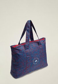 Gran bolsa tote en azul con un patrón salpicado en rojo, material de tela, asas resistentes y detalle de logo circular en el frente.