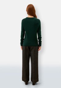 Dunkelgrüner Pullover mit rundem Halsausschnitt, gerippten Bündchen und Saum, kombiniert mit weiten, dunkelblauen Jeans mit sichtbar genähten Nähten.