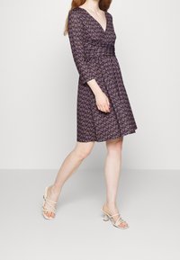 Lila klänning med lång ärm, mönstrad med små blommönster i gult och grönt. Matchad med ljusa klackar med remmar.