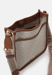 Beige lærredstaske med monogram mønster og brune læderdetaljer. Har en brun justerbar rem og en magnetisk tryklås.