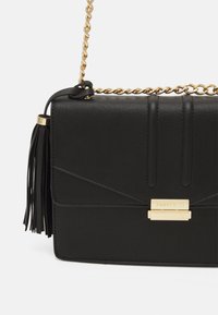 Borsa a tracolla in pelle nera con catena dorata, caratterizzata da una chiusura dorata, dettaglio con nappina e cuciture diagonali sulla parte anteriore.