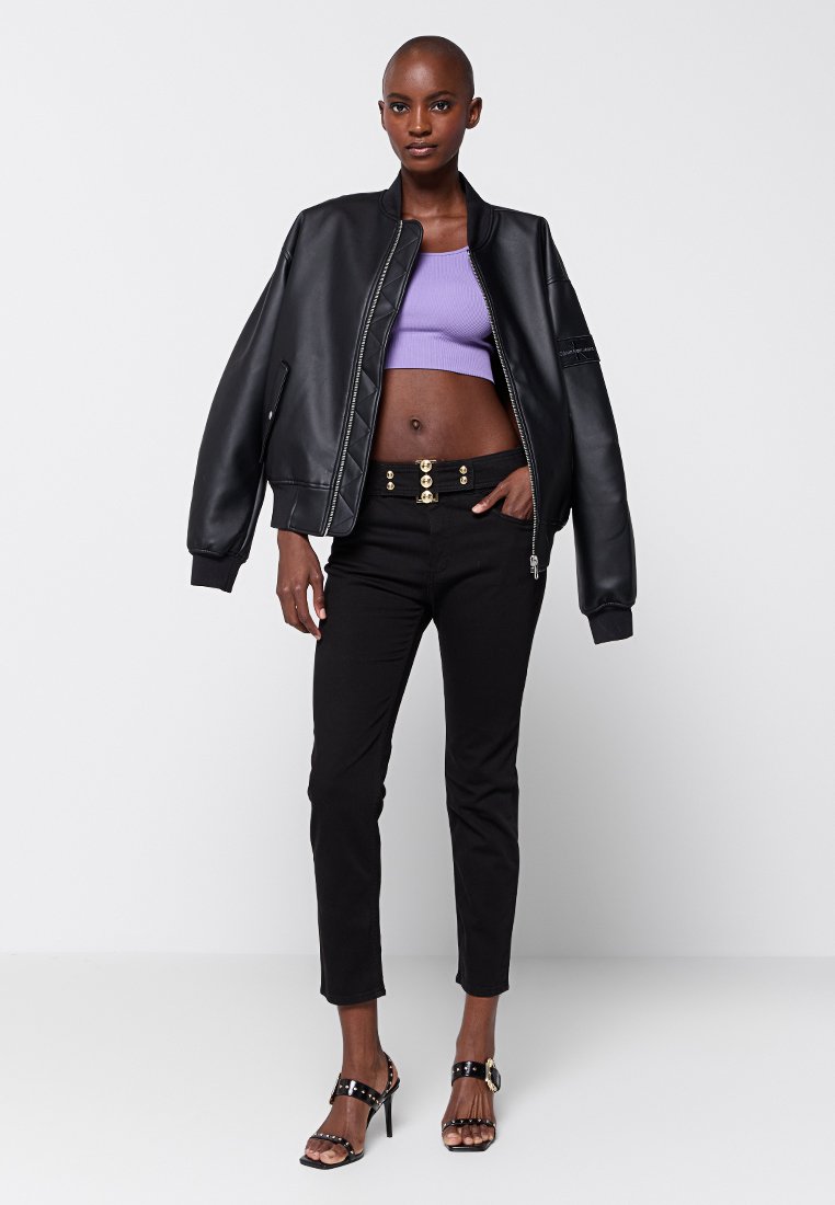 Czarna bomberka z sztucznej skóry, fioletowy krótki top, czarne obcisłe spodnie z detalem złotych guzików oraz czarne sandały na obcasie. Prosty design, nowoczesny wygląd.