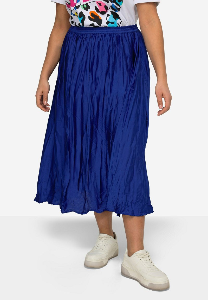 Falda plisada azul de largo medio, hecha de una tela ligera y brillante. Presenta una cinturilla elástica y una silueta fluida. Se lleva con zapatillas blancas.
