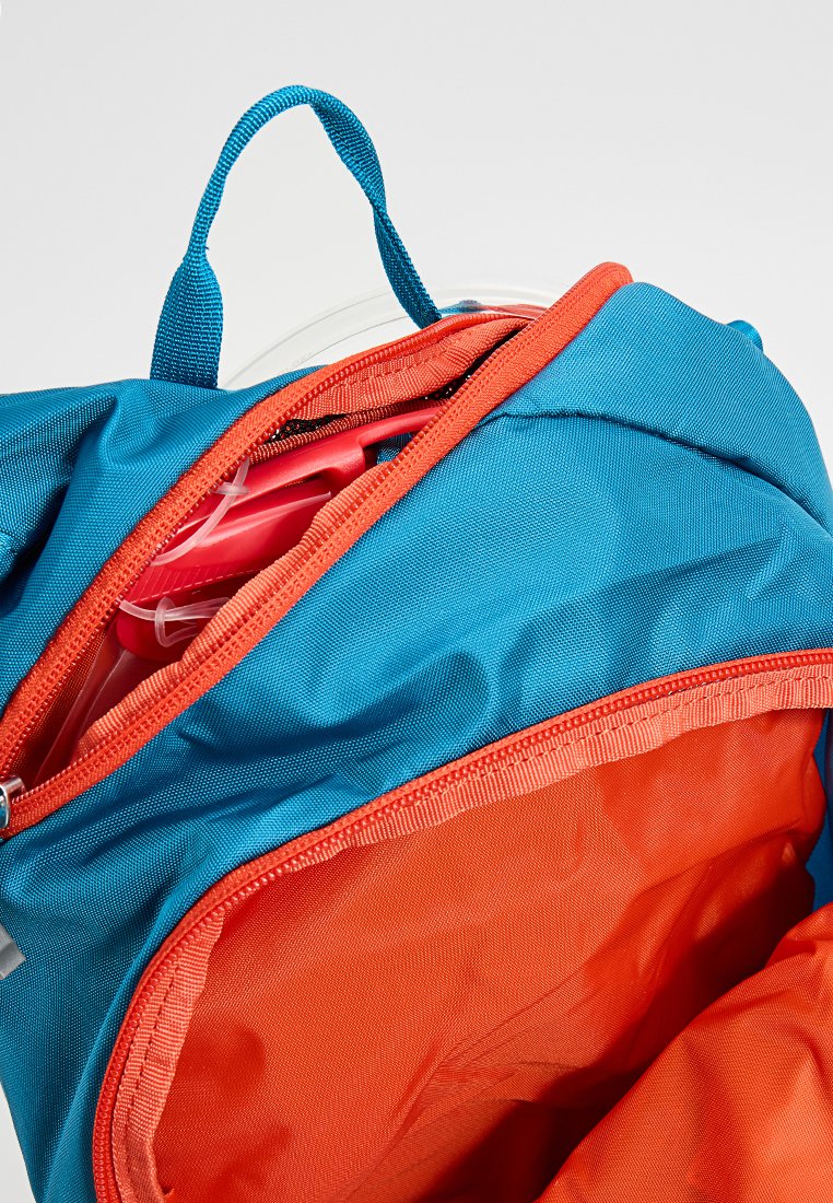 Blå och orange ryggsäcksinredning med dragkedja, som visar mjukt tyg, flera fickor och ett synligt hårt föremål i rött.