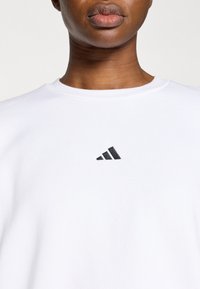 Λευκό φούτερ από βαμβακερό μείγμα, με στρογγυλή λαιμόκοψη και μικρό μαύρο τρίγωνο λογότυπο στο στήθος. Μαλακή υφή.