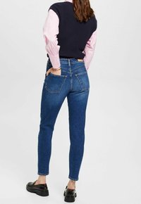 Vaqueros de mezclilla azul oscuro de tiro alto, con un ajuste ceñido, bolsillos traseros y un ligero estiramiento para mayor comodidad. Combinados con un chaleco azul marino.