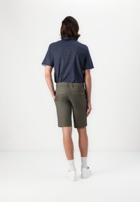Navyblaues kurzärmeliges Hemd mit geometrischem Muster, kombiniert mit olivgrünen Shorts. Der Look wird mit weißen Turnschuhen und Socken in Crew-Länge abgerundet.